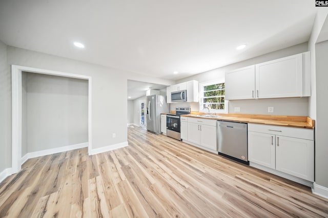 kitchen featuring butcher block countertops, appliances with stainless steel finishes, white cabinets, light hardwood / wood-style flooring, and sink