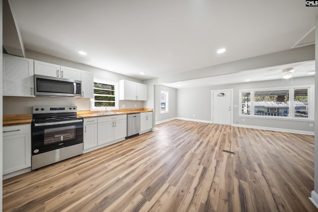 kitchen featuring white cabinetry, butcher block counters, appliances with stainless steel finishes, a healthy amount of sunlight, and light wood-type flooring