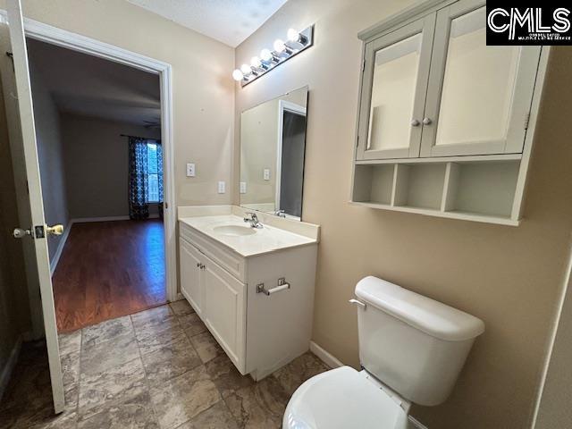 half bath featuring baseboards, vanity, and toilet