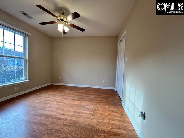 empty room with a ceiling fan, wood finished floors, visible vents, and baseboards