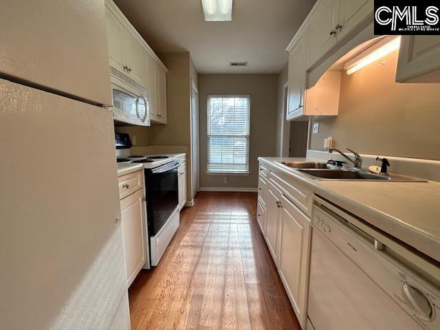 kitchen featuring light countertops, light wood-style flooring, white cabinetry, a sink, and white appliances