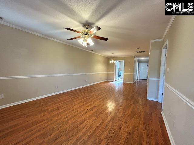 unfurnished living room featuring dark wood-style flooring, crown molding, baseboards, and ceiling fan with notable chandelier