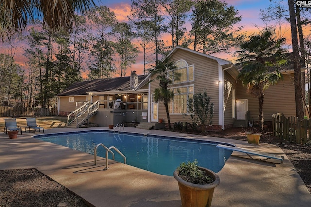 pool at dusk with a patio area and a diving board