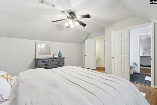 bedroom featuring a textured ceiling, dark wood-type flooring, connected bathroom, vaulted ceiling, and ceiling fan