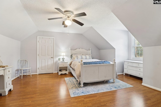 bedroom featuring ceiling fan, wood-type flooring, vaulted ceiling, and a textured ceiling