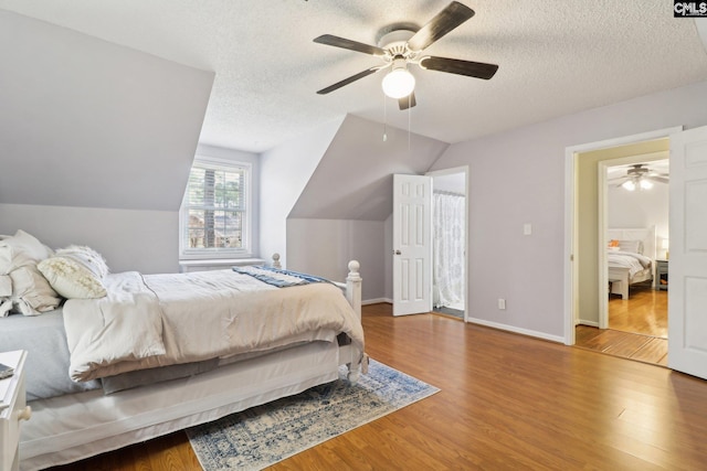 bedroom with ceiling fan, wood-type flooring, a textured ceiling, and lofted ceiling