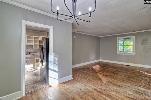 unfurnished dining area featuring an inviting chandelier, crown molding, wood-type flooring, and sink