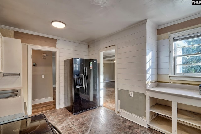 kitchen with sink, crown molding, wood walls, and black fridge with ice dispenser