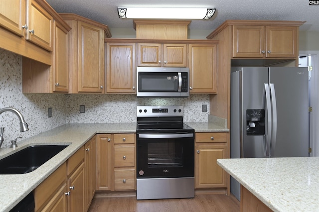 kitchen featuring backsplash, sink, light wood-type flooring, light stone countertops, and appliances with stainless steel finishes