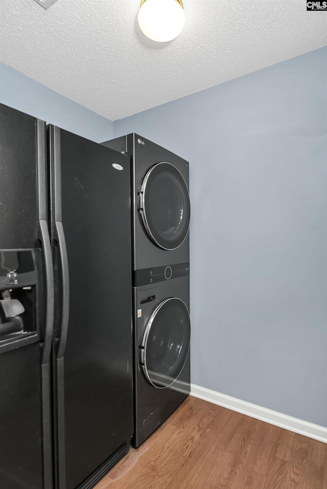 laundry area featuring wood-type flooring, stacked washer and clothes dryer, and a textured ceiling