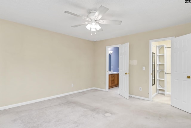 unfurnished bedroom with light carpet, ceiling fan, ensuite bath, a closet, and a walk in closet