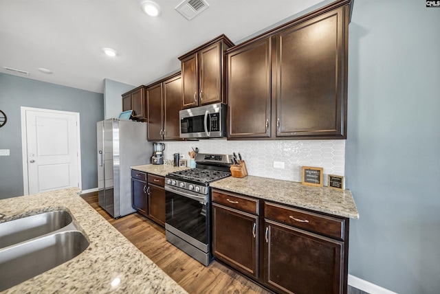 kitchen featuring backsplash, light hardwood / wood-style floors, appliances with stainless steel finishes, dark brown cabinets, and light stone counters