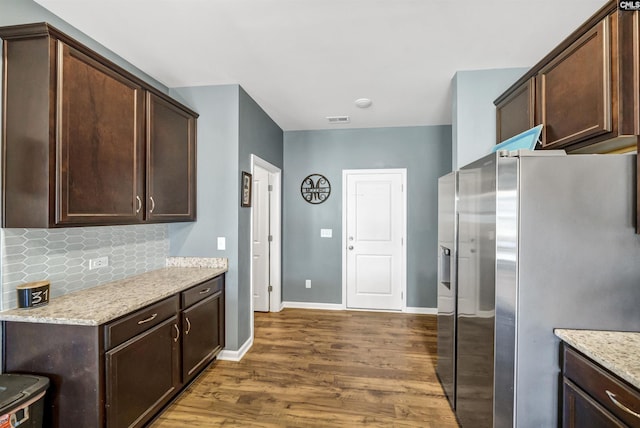 kitchen with stainless steel fridge with ice dispenser, dark hardwood / wood-style flooring, dark brown cabinetry, and light stone countertops