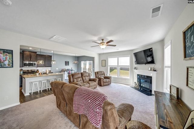 living room with dark colored carpet, a fireplace, and ceiling fan