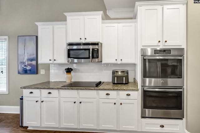 kitchen with white cabinets, stainless steel appliances, tasteful backsplash, dark stone countertops, and ornamental molding