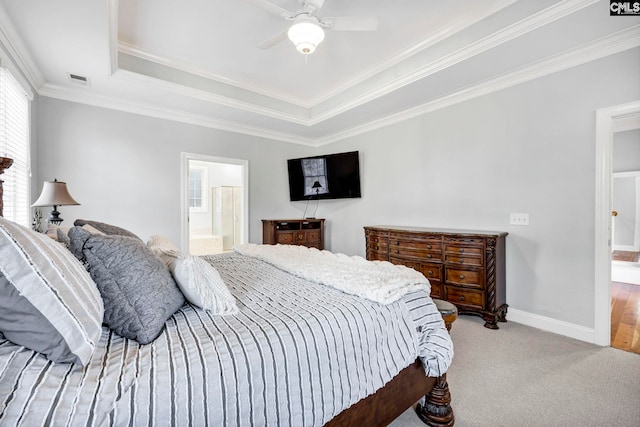 carpeted bedroom featuring ceiling fan, ornamental molding, a raised ceiling, and ensuite bath