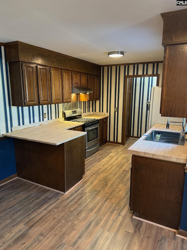 kitchen with gas stove, wood-type flooring, white fridge, sink, and kitchen peninsula