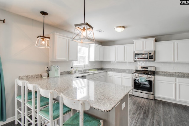 kitchen with white cabinetry, stainless steel appliances, sink, hanging light fixtures, and a breakfast bar area