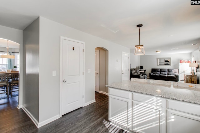 kitchen with dark wood-type flooring, light stone countertops, white cabinetry, and hanging light fixtures