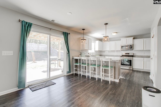 kitchen with white cabinets, appliances with stainless steel finishes, decorative backsplash, hanging light fixtures, and a breakfast bar