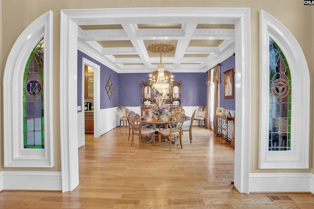 dining area featuring an inviting chandelier, light hardwood / wood-style floors, coffered ceiling, crown molding, and beam ceiling