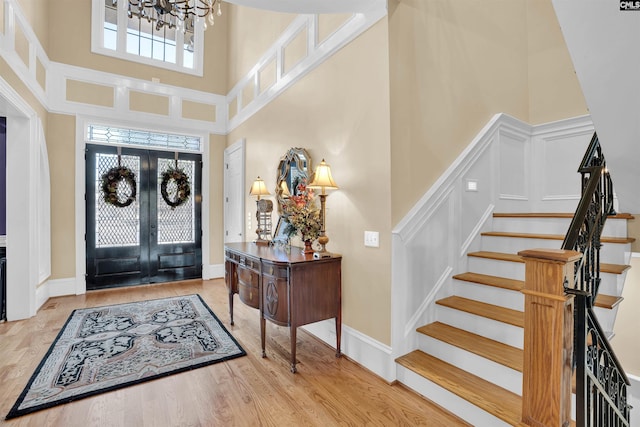 foyer entrance featuring french doors, a high ceiling, a chandelier, and light hardwood / wood-style flooring