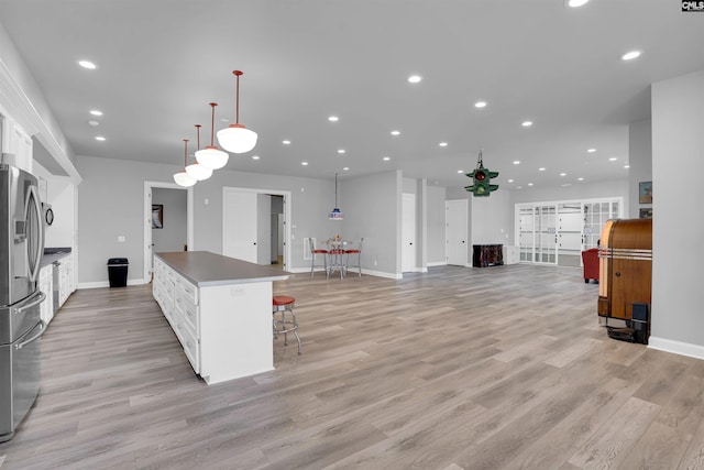 kitchen featuring white cabinetry, stainless steel fridge, hanging light fixtures, a breakfast bar, and a center island