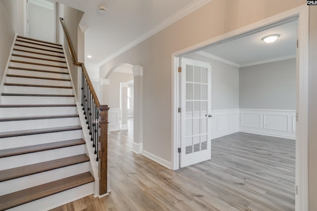 stairway with arched walkways, crown molding, a decorative wall, and wood finished floors