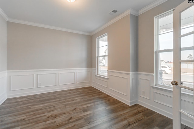 empty room featuring a wainscoted wall, crown molding, visible vents, and wood finished floors