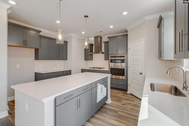 kitchen featuring stainless steel appliances, a sink, light wood-style floors, wall chimney range hood, and a center island