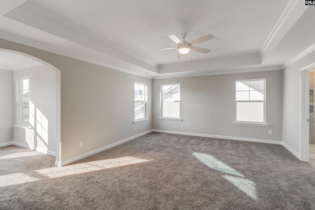 empty room featuring arched walkways, a raised ceiling, baseboards, and carpet