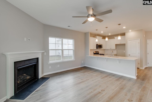 kitchen featuring stainless steel appliances, light countertops, a fireplace with raised hearth, a sink, and a peninsula