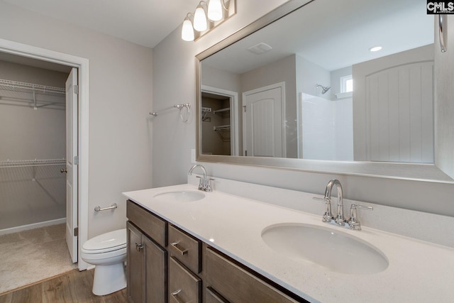 full bath featuring double vanity, tiled shower, a sink, and toilet