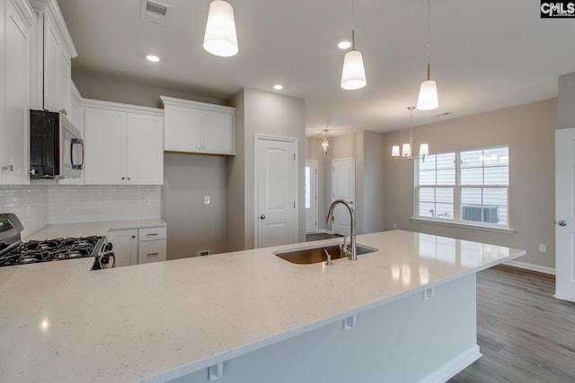 kitchen with light stone counters, stainless steel microwave, visible vents, a sink, and gas range