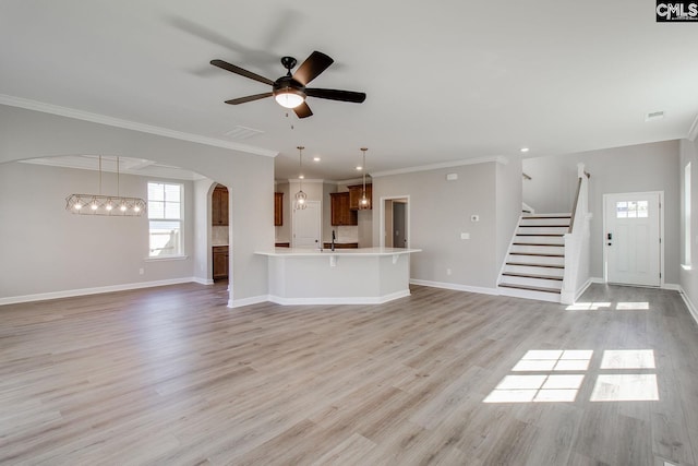 unfurnished living room featuring arched walkways, light wood-style flooring, ceiling fan with notable chandelier, stairway, and crown molding