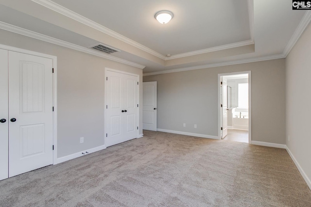 unfurnished bedroom with carpet floors, visible vents, baseboards, multiple closets, and a raised ceiling