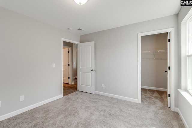 unfurnished bedroom with carpet, a spacious closet, and baseboards