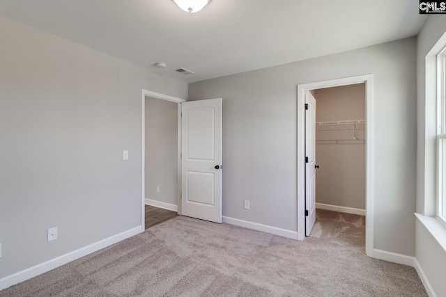 unfurnished bedroom with baseboards, visible vents, a walk in closet, carpet flooring, and a closet