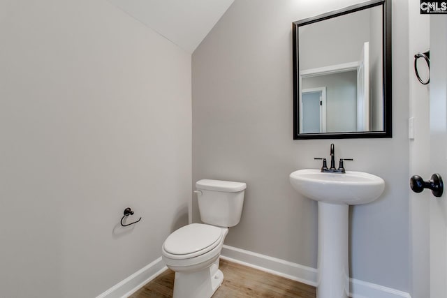 bathroom featuring toilet, a sink, wood finished floors, baseboards, and vaulted ceiling