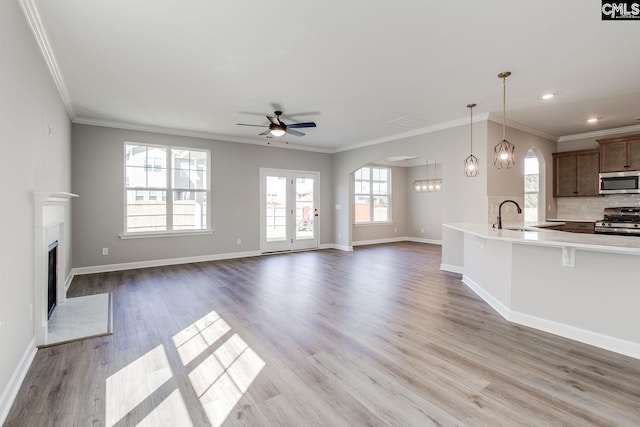 unfurnished living room with a fireplace with flush hearth, ornamental molding, a sink, wood finished floors, and baseboards