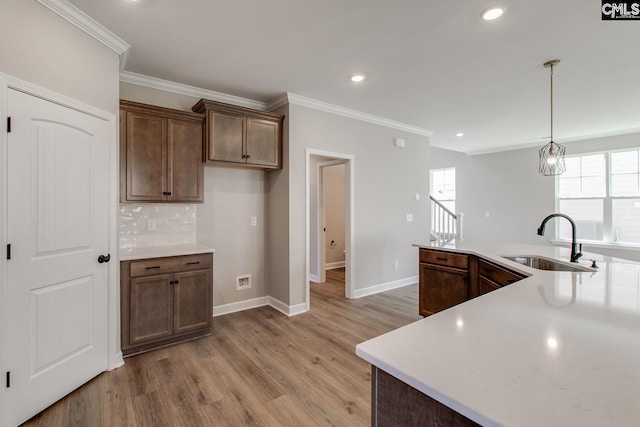 kitchen featuring light wood-style flooring, a sink, light countertops, tasteful backsplash, and crown molding