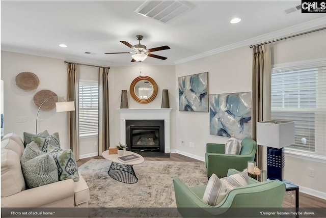 living room with ceiling fan, wood finished floors, visible vents, ornamental molding, and a glass covered fireplace