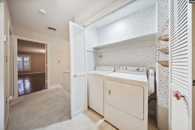 laundry room with washing machine and clothes dryer, light colored carpet, and a textured ceiling