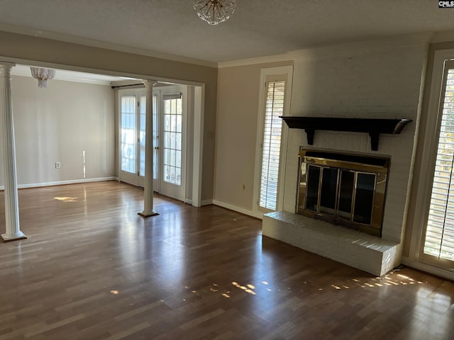 unfurnished living room with dark wood-type flooring, ornate columns, a textured ceiling, ornamental molding, and a fireplace