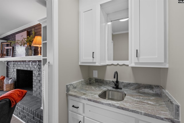 bar featuring white cabinetry, a fireplace, sink, light stone counters, and crown molding