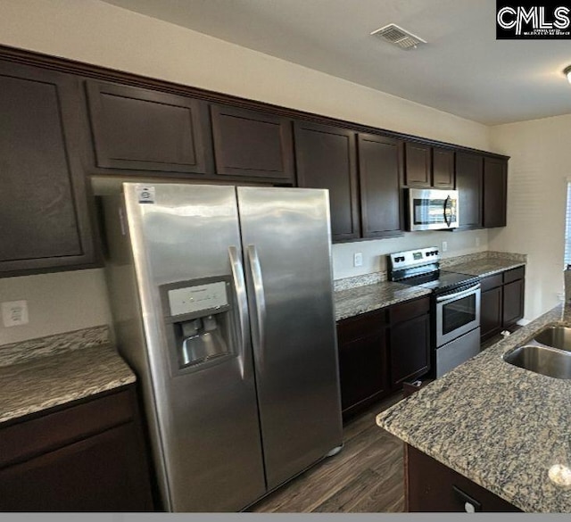 kitchen featuring light stone countertops, dark brown cabinetry, dark hardwood / wood-style flooring, stainless steel appliances, and sink