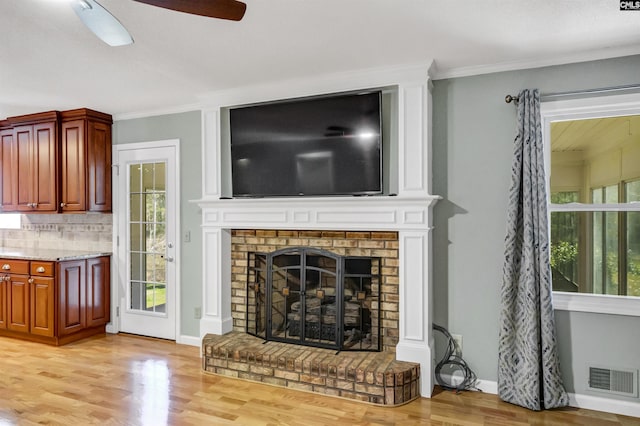 living room with ceiling fan, ornamental molding, light hardwood / wood-style flooring, and a brick fireplace