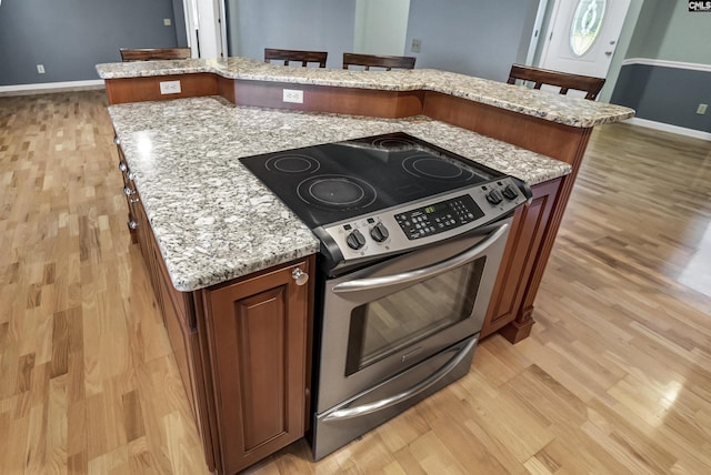 kitchen featuring light stone countertops, electric stove, a breakfast bar, and light hardwood / wood-style floors