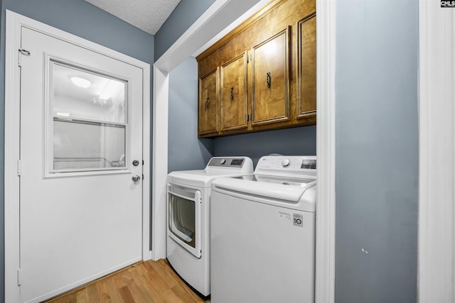 laundry area with a textured ceiling, cabinets, washing machine and clothes dryer, and light wood-type flooring