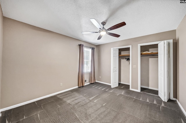 unfurnished bedroom featuring a textured ceiling, ceiling fan, dark carpet, and multiple closets